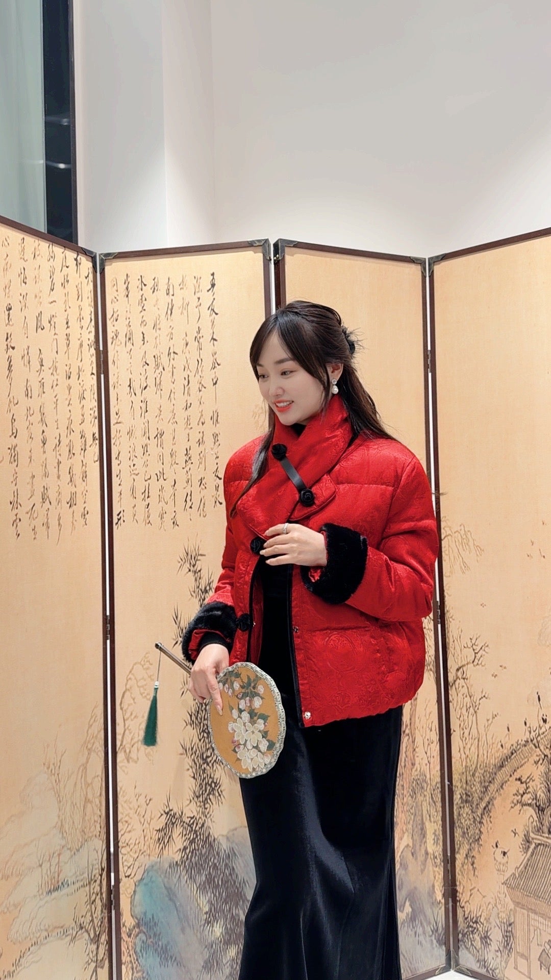 Woman in a red jacket standing in front of an ornate screen with artistic designs.