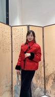 Woman wearing a red coat standing in front of a decorative screen with Chinese characters.