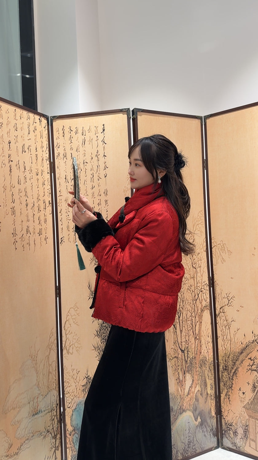 Woman in a red coat holding a pen in front of an ornate screen with artistic designs.