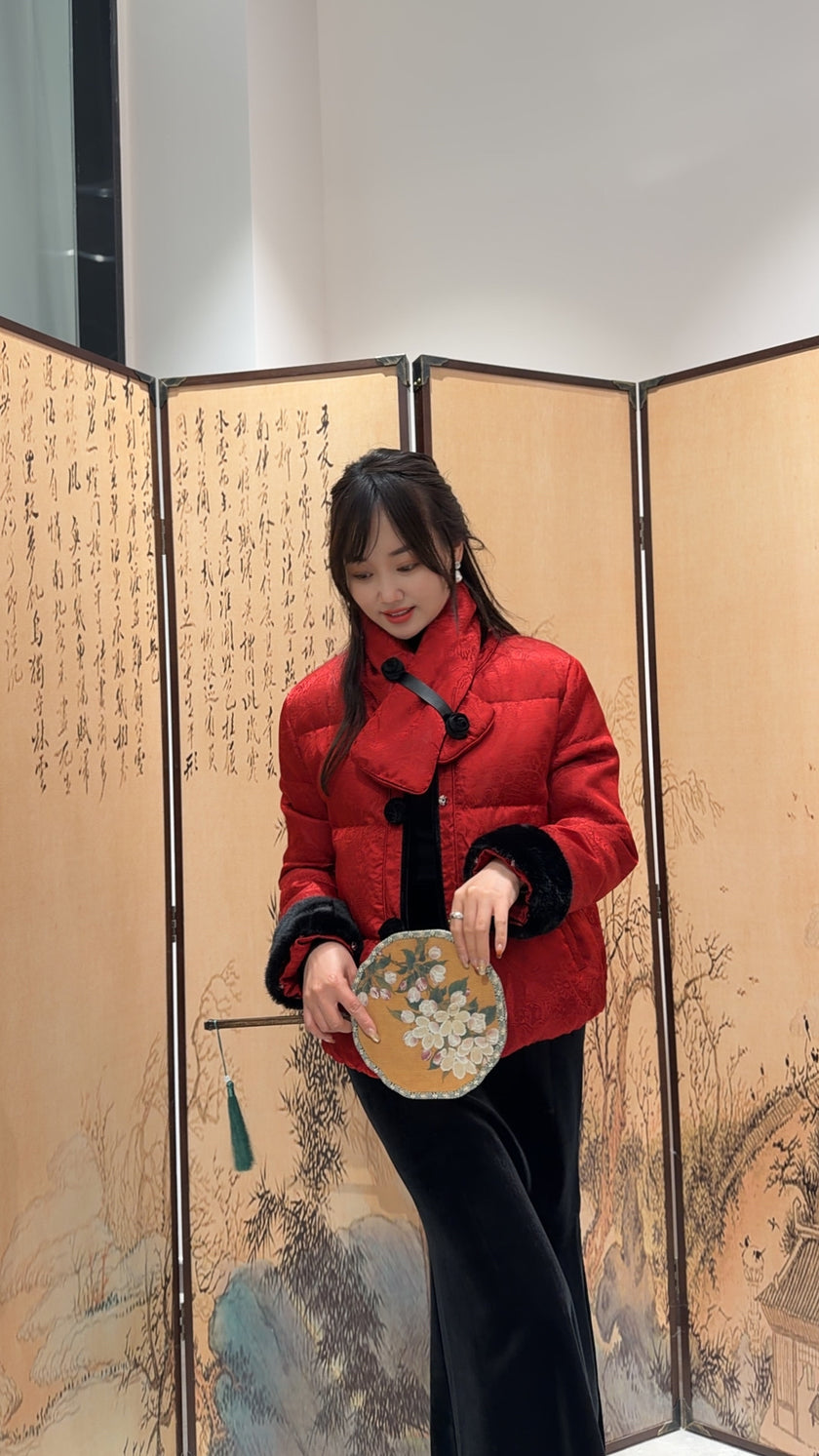 Woman in a red coat holding a round object in front of an ornate screen.