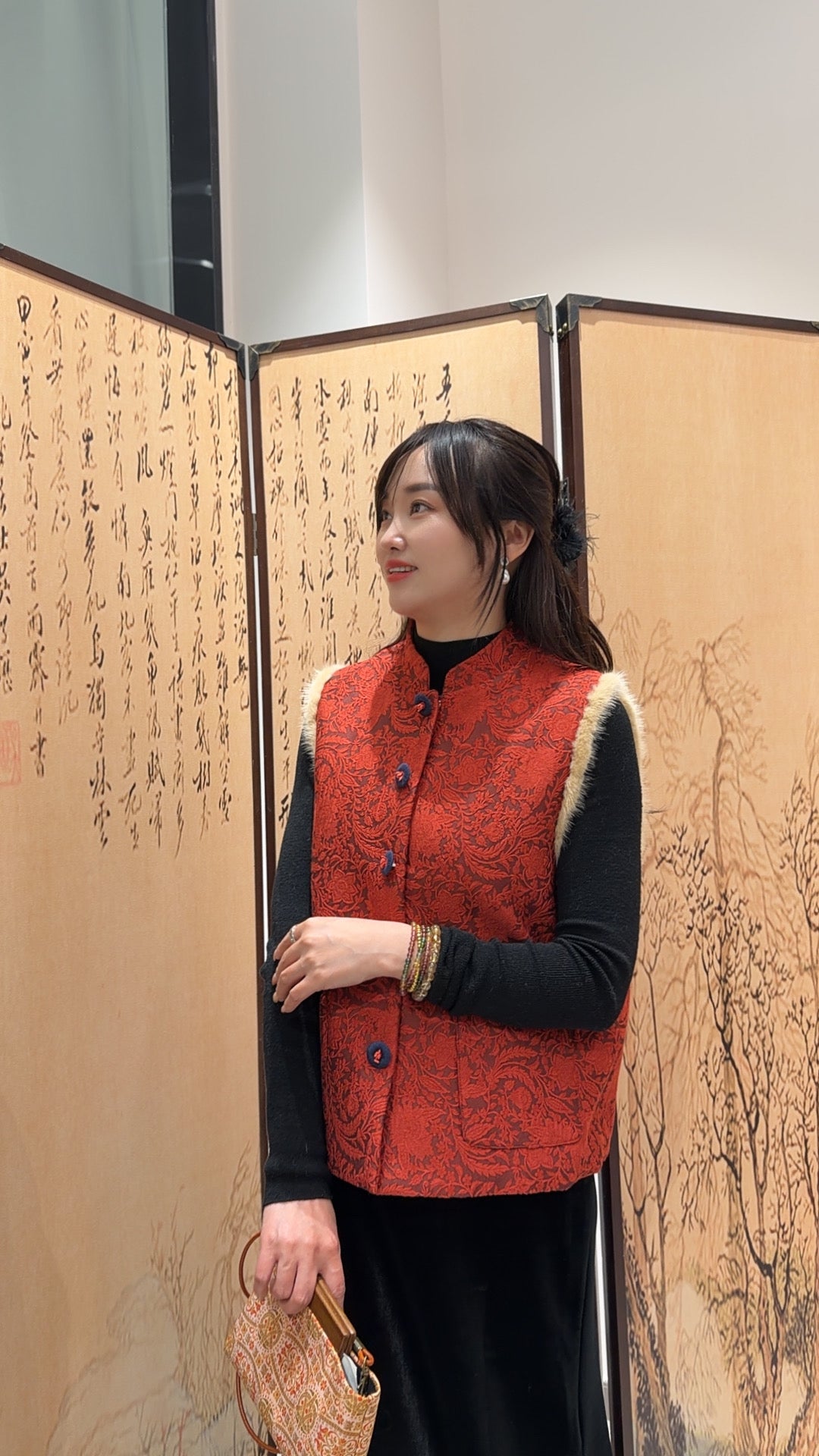 Woman wearing a red patterned vest standing in front of an open screen with Chinese characters.