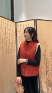 Woman wearing a red patterned vest standing in front of an open screen with Chinese characters.
