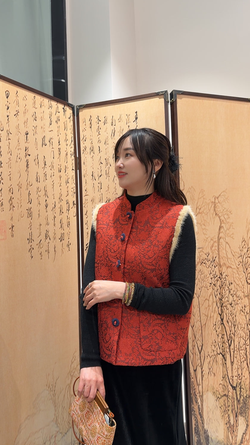 Woman wearing a red patterned vest standing in front of an open screen with Chinese characters.