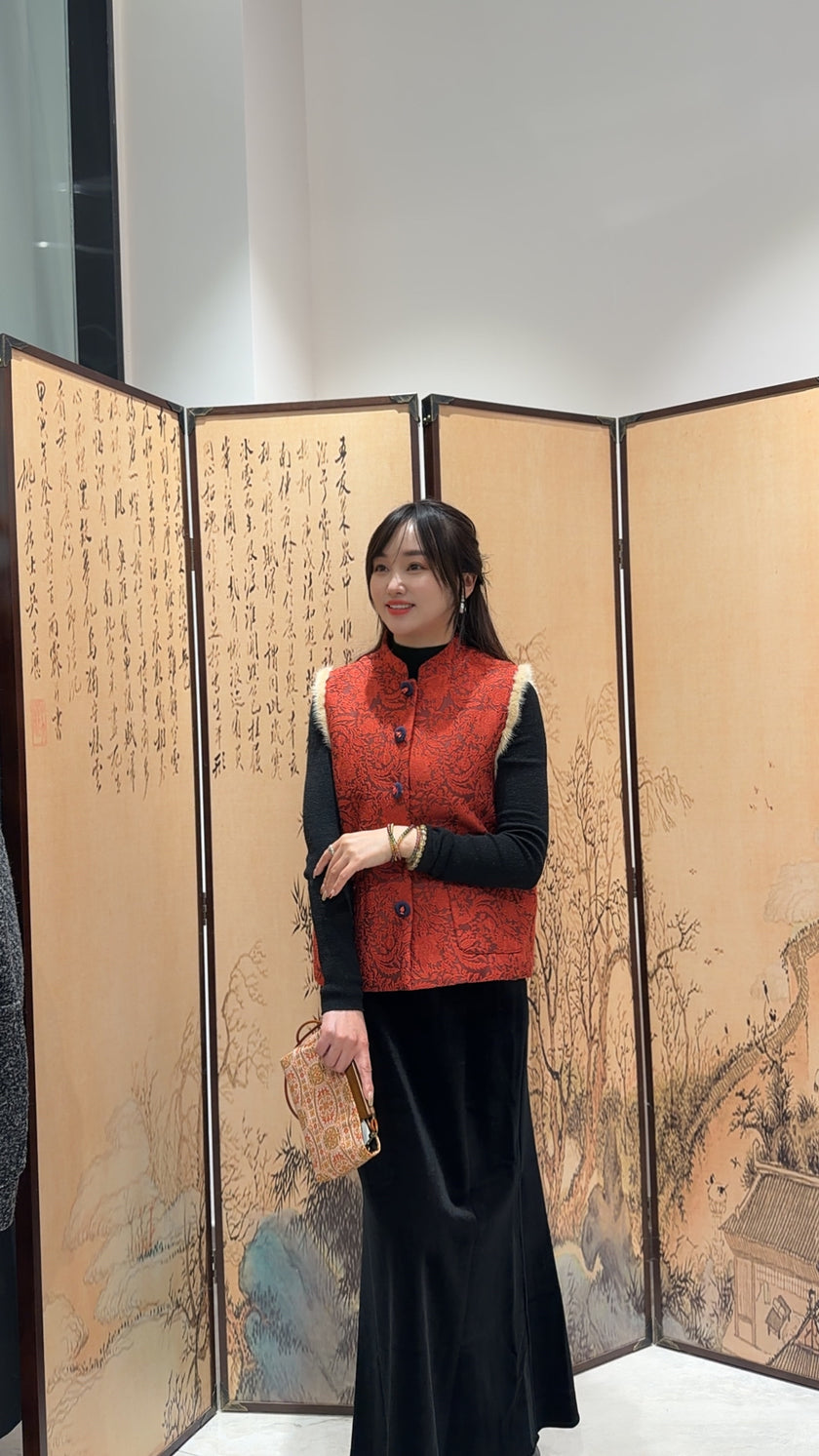 Woman in a red vest standing in front of an artistic screen with traditional designs.