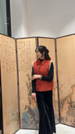 Woman in a red vest standing in front of an artistic screen with traditional designs.