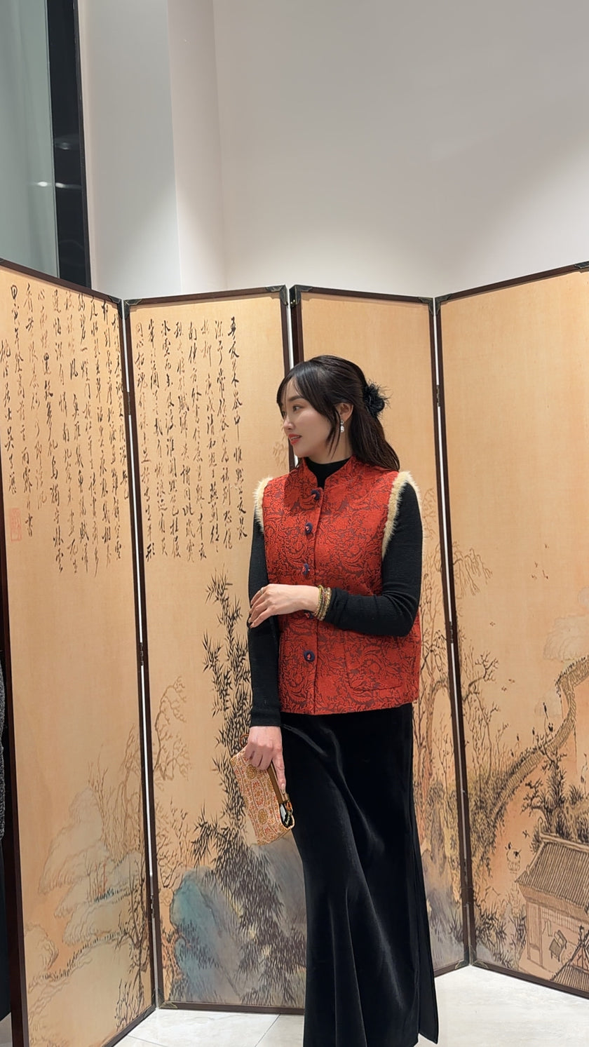 Woman in a red vest standing in front of an artistic screen with traditional designs.