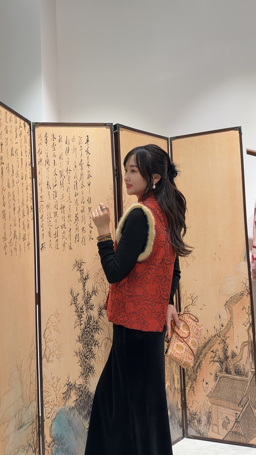 Woman in a red vest standing in front of an ornate screen with artistic designs.