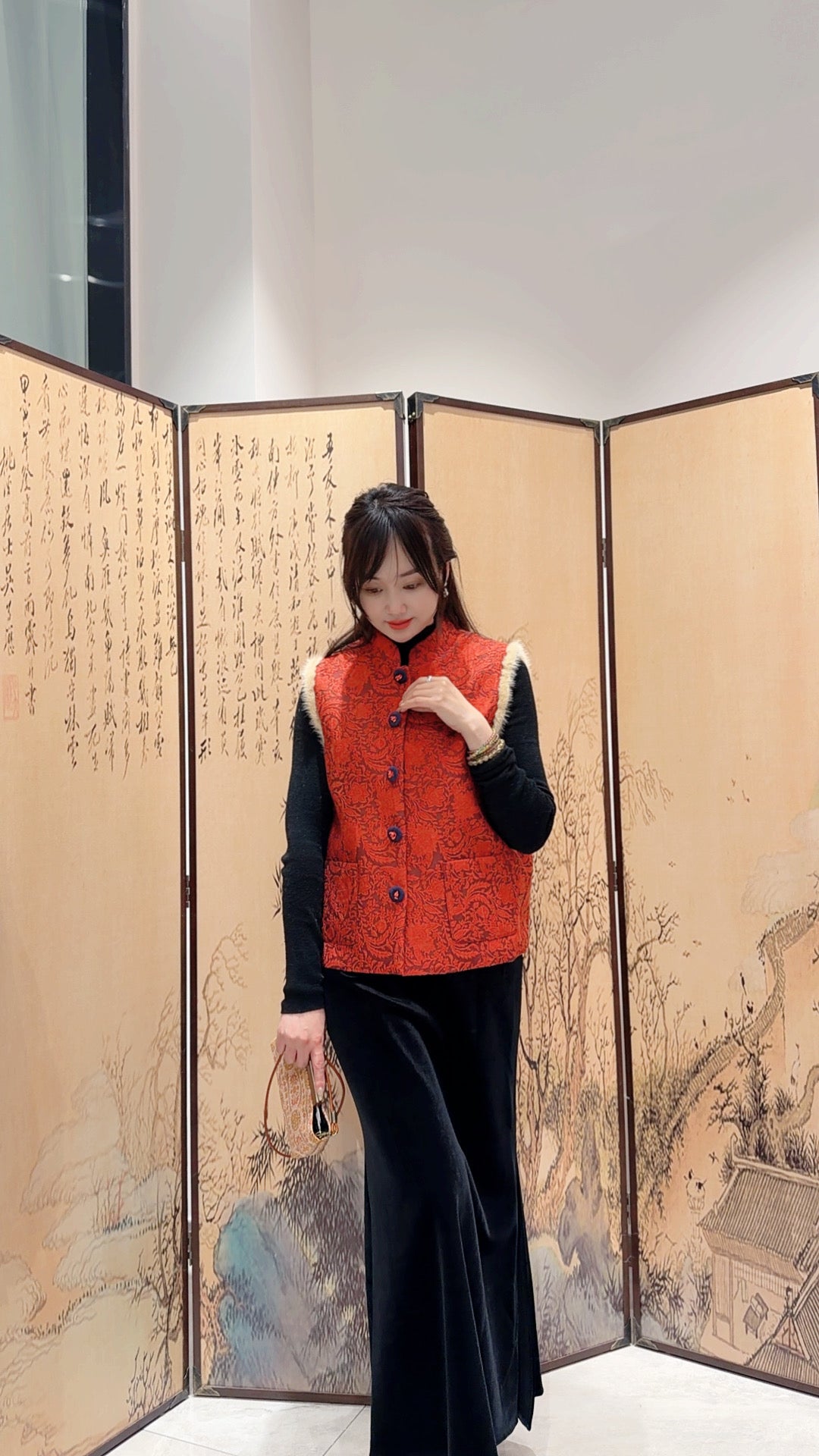 Woman in a red vest standing in front of a decorative screen with artistic designs.