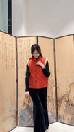 Woman in a red vest standing in front of a decorative screen with artistic designs.