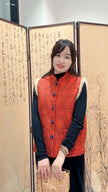 Woman wearing a red patterned vest standing in front of a decorative screen.