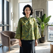 Woman in a green mulberry silk blouse standing in a modern living room.