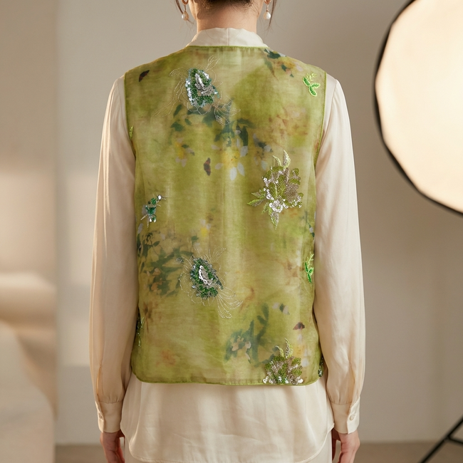 Person wearing a green sequin embroidered vest over a white shirt with a neutral background