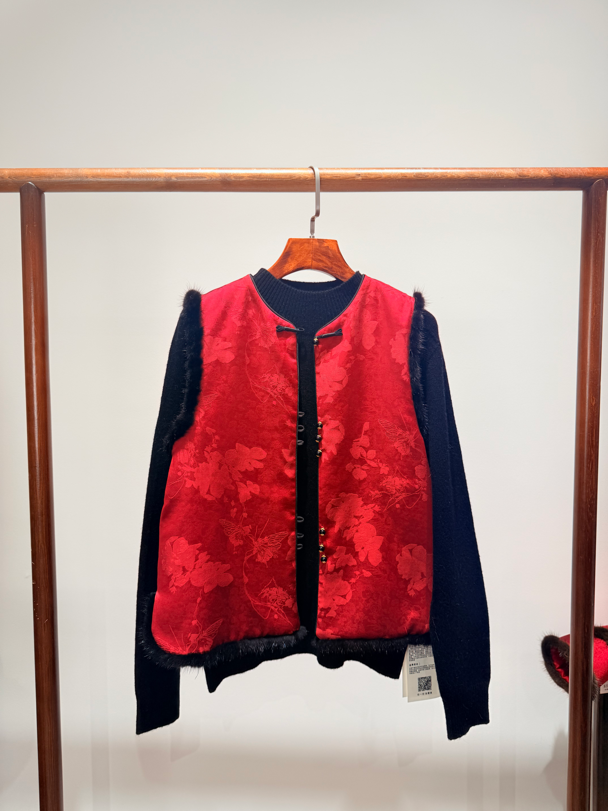 Red and black vest hanging on a wooden rack against a white wall.