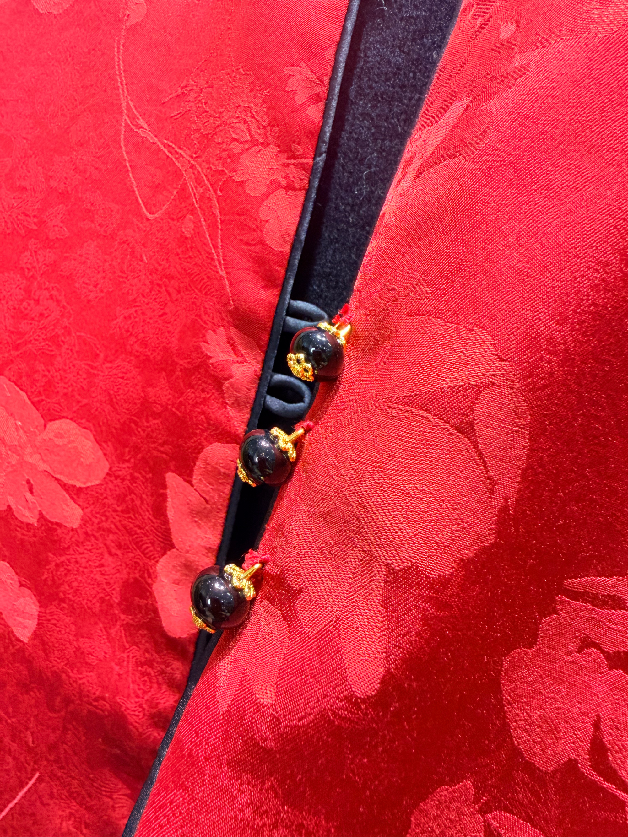 Close-up of a red fabric with floral patterns and a black cord with beads.