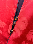 Close-up of a red fabric with floral patterns and a black cord with beads.