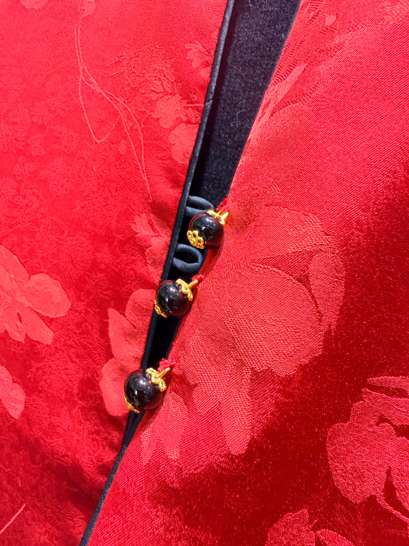 Close-up of a red fabric with floral patterns and a black cord with beads.
