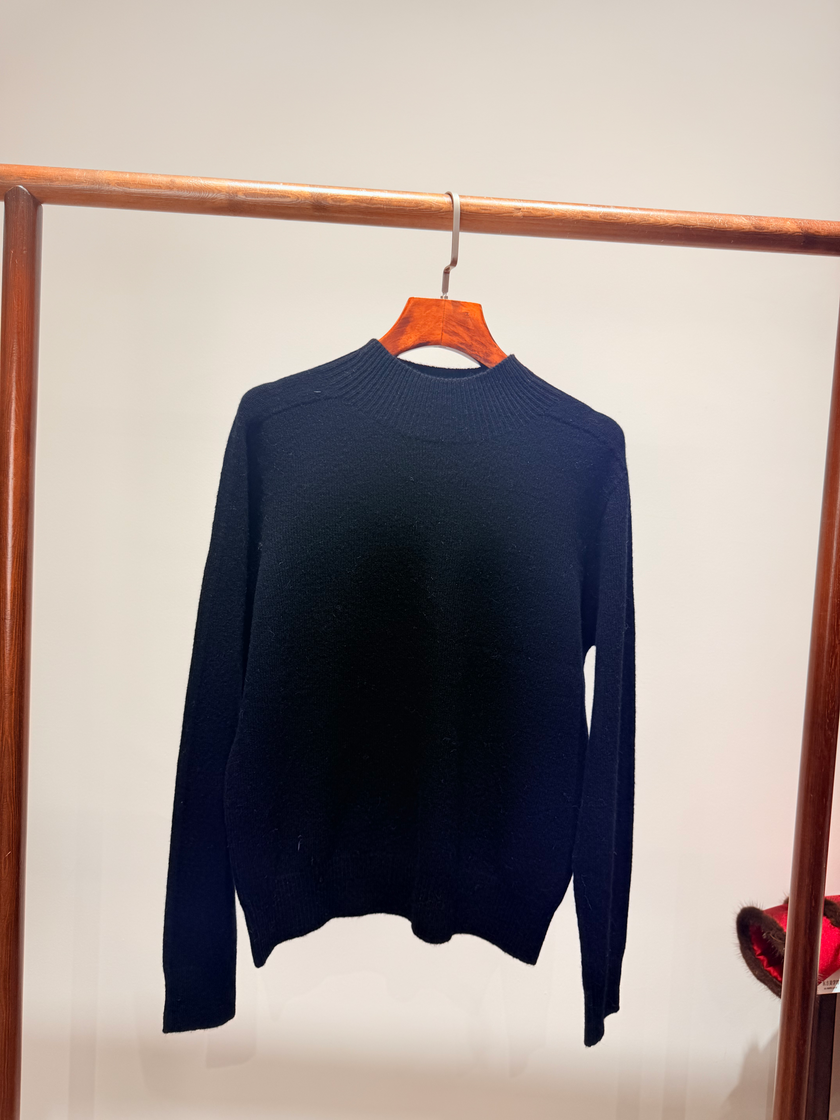 Navy blue sweater hanging on a wooden rack against a plain background