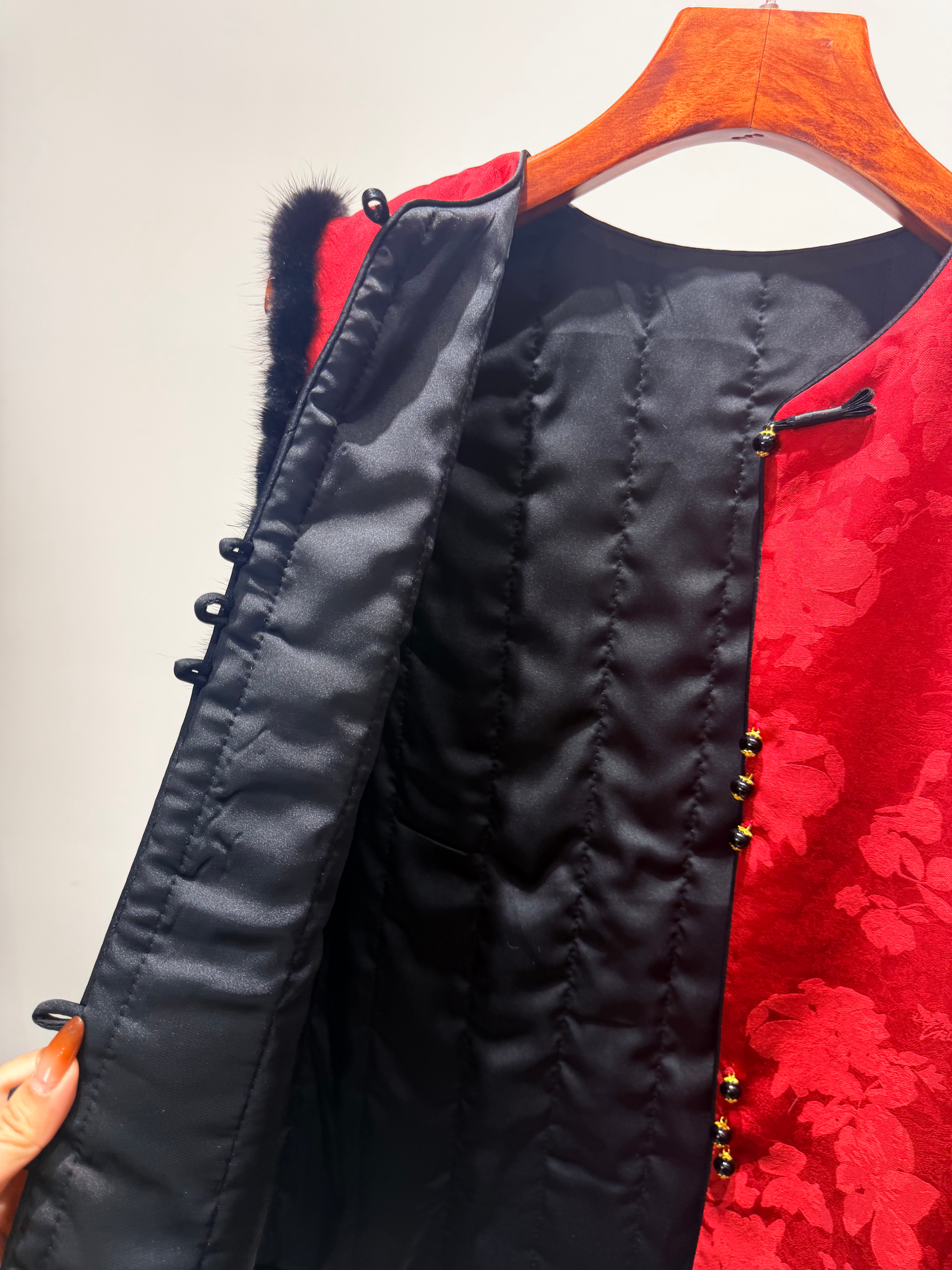 Red and black jacket with floral pattern on a hanger against a plain background