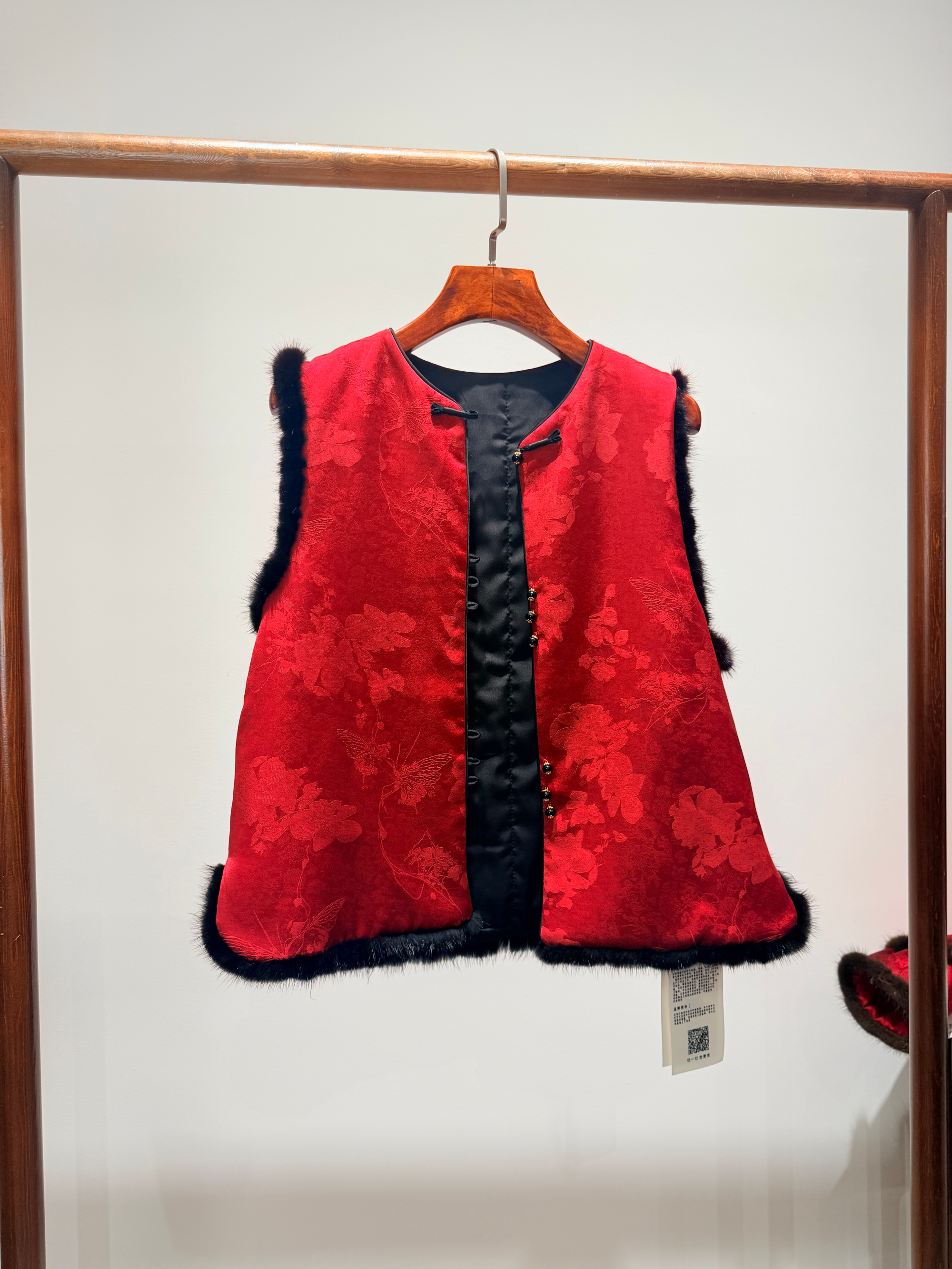 Red vest with black trim on a hanger against a white wall