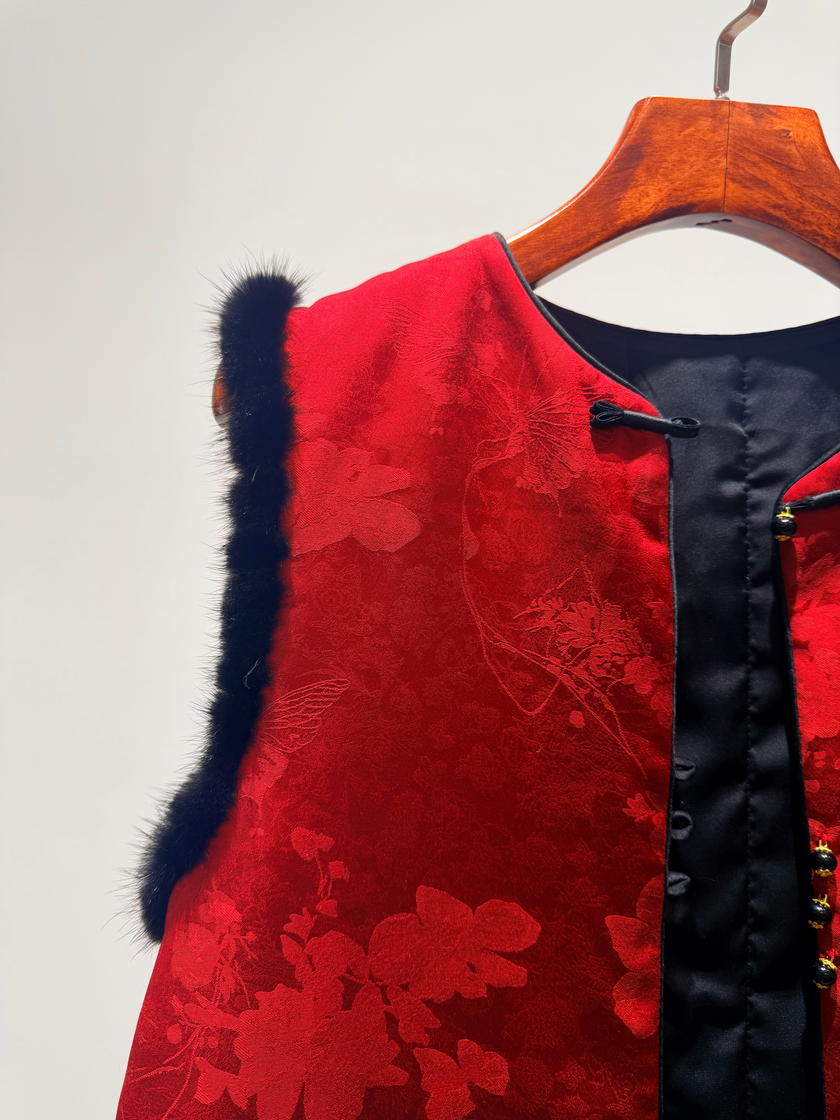 Red floral-patterned garment with black fur trim on a wooden hanger against a white background