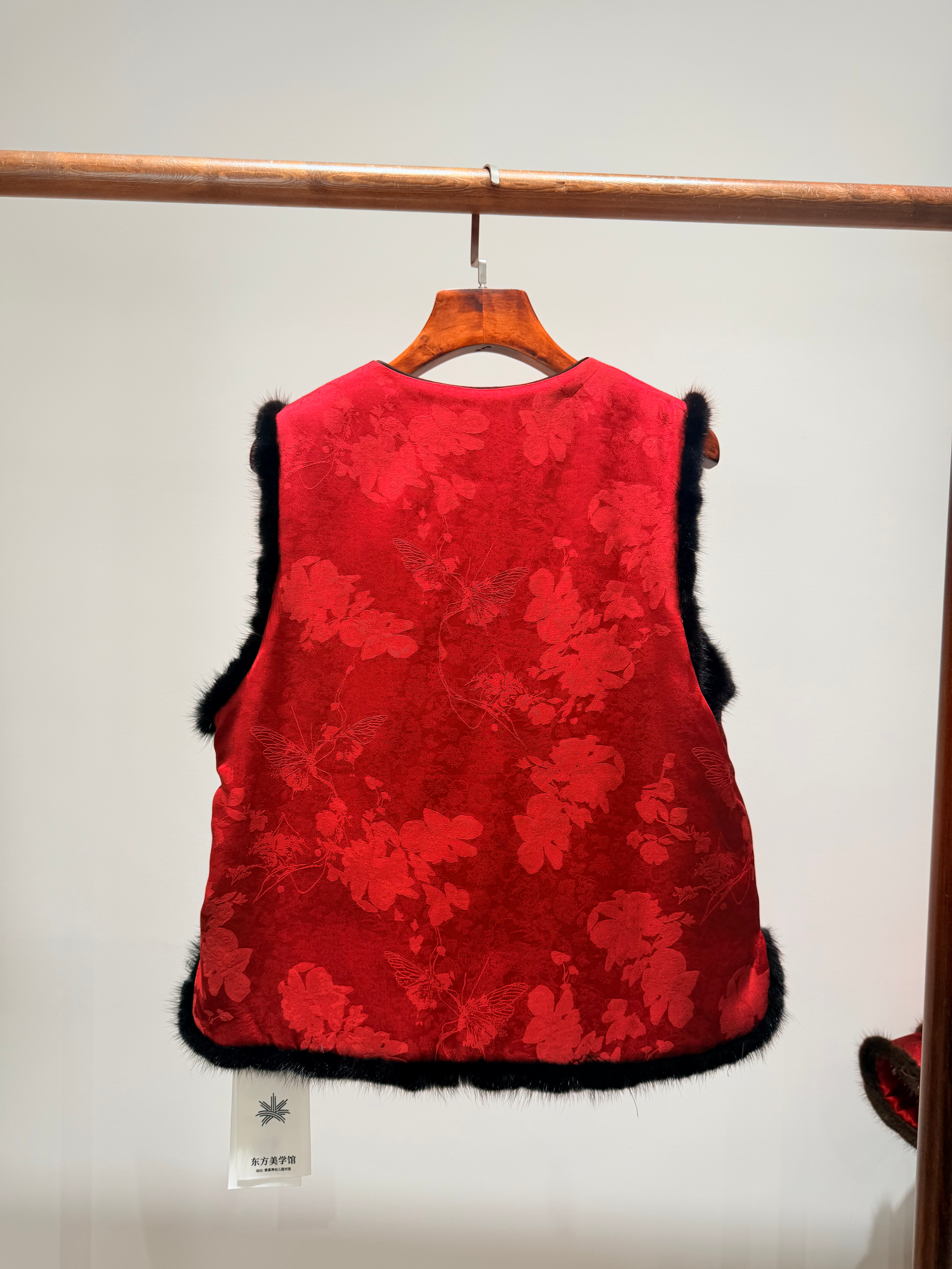 Red floral-patterned vest with black trim on a hanger against a white background