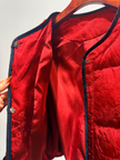 Red quilted jacket with navy trim on a hanger against a white background