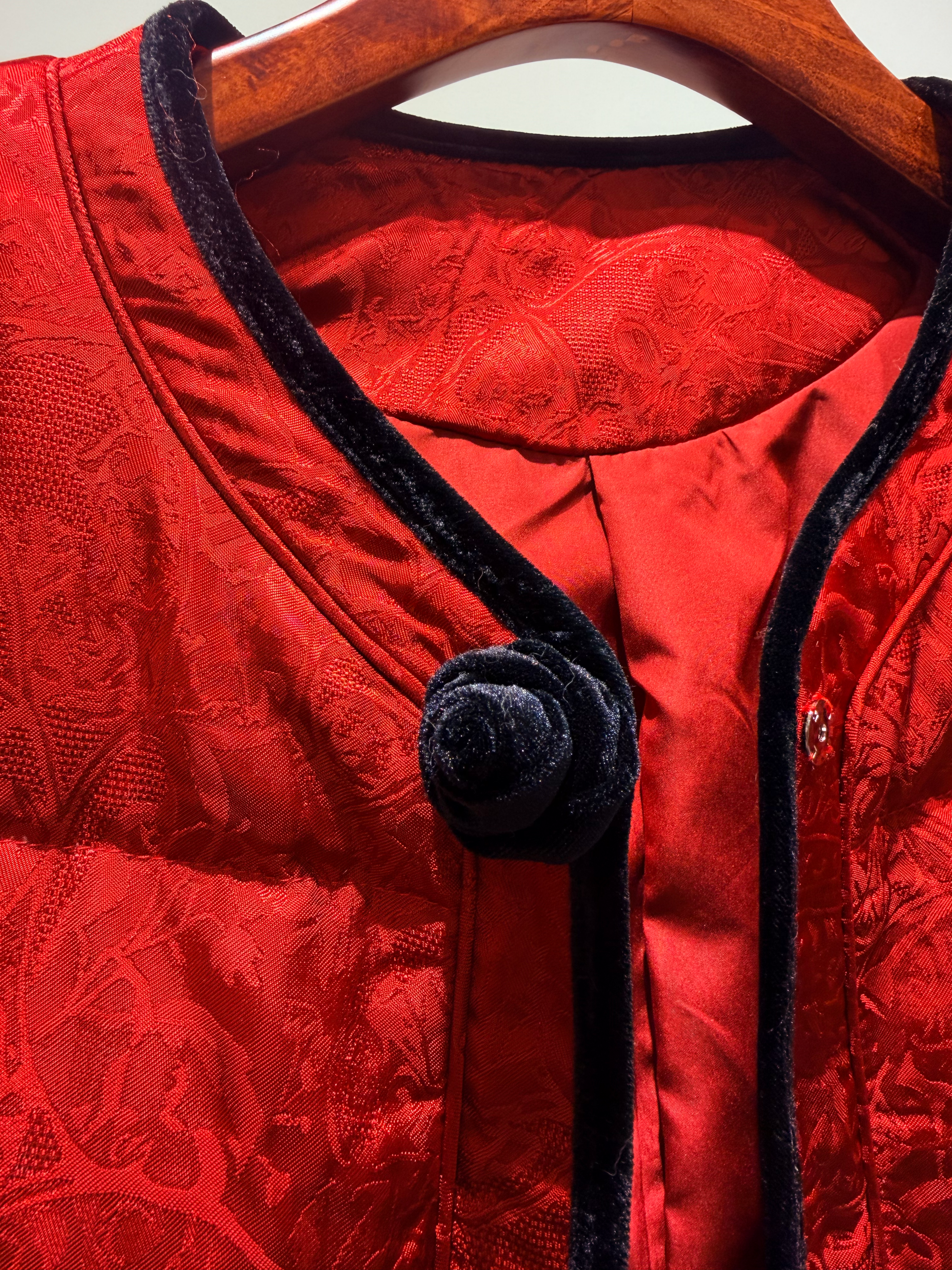 Red jacket with black lace trim and buttons on a hanger