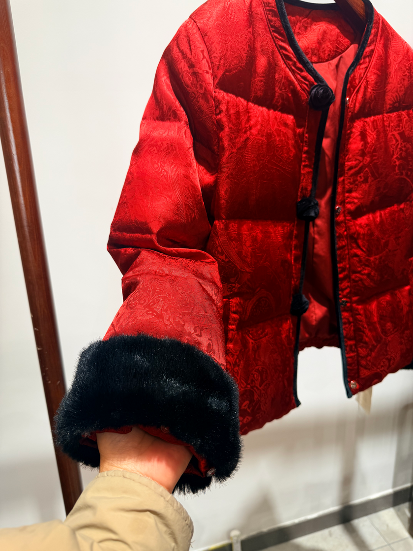 Red puffer jacket with black fur trim on a hanger against a white background