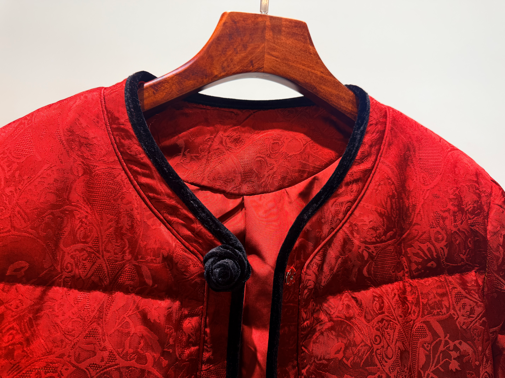 Red garment with black trim on a wooden hanger against a white background