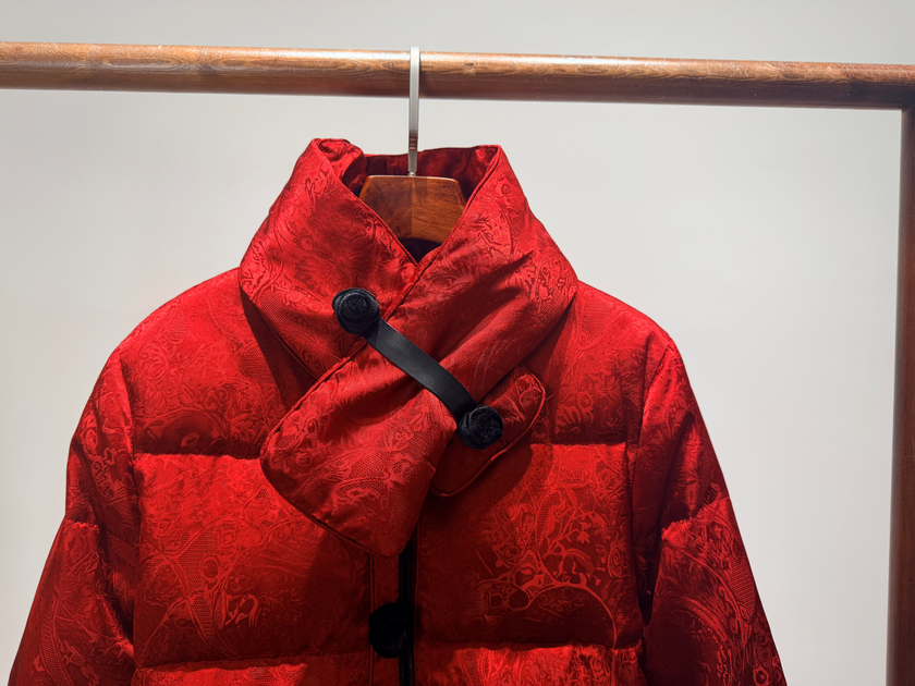 Red puffer jacket with black buttons on a hanger against a light gray background