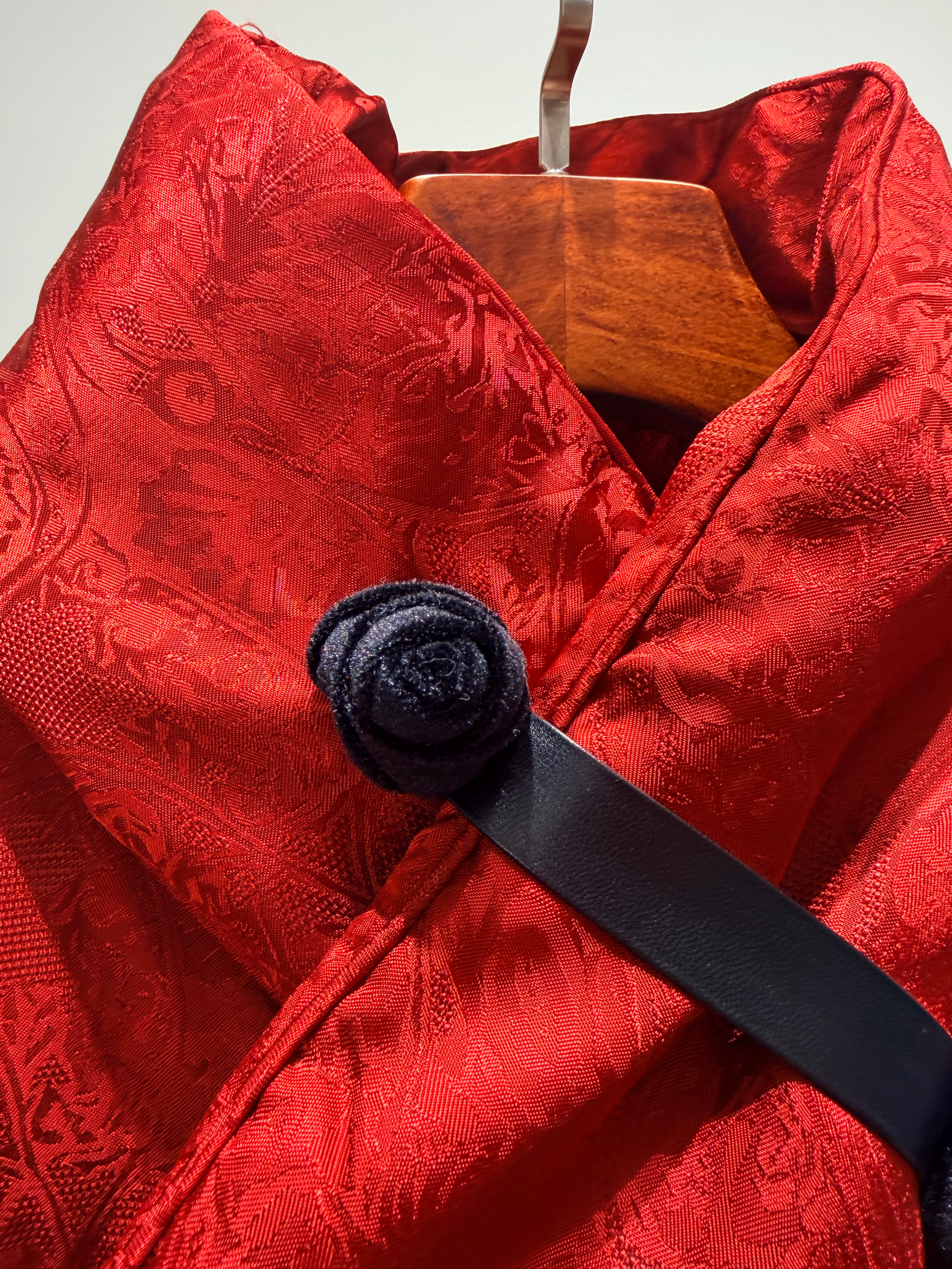 Red textured garment with a black belt and wooden hanger on a light gray background
