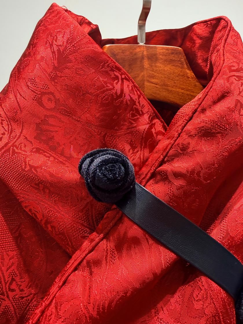 Red textured garment with a black belt and wooden hanger on a light gray background