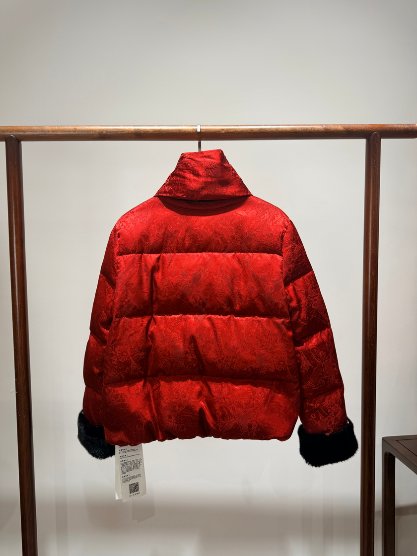 Red puffer jacket with black fur trim on a wooden rack against a white background