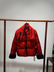 Red puffer jacket with black trim hanging on a rack against a plain background