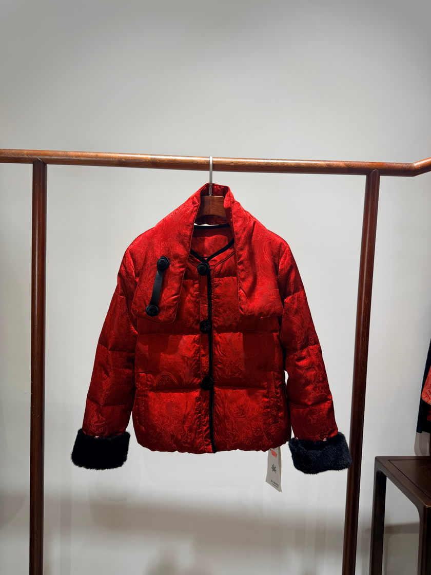 Red puffer jacket with black trim hanging on a rack against a plain background