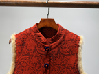 Red textured vest with fur trim on a wooden hanger against a gray background