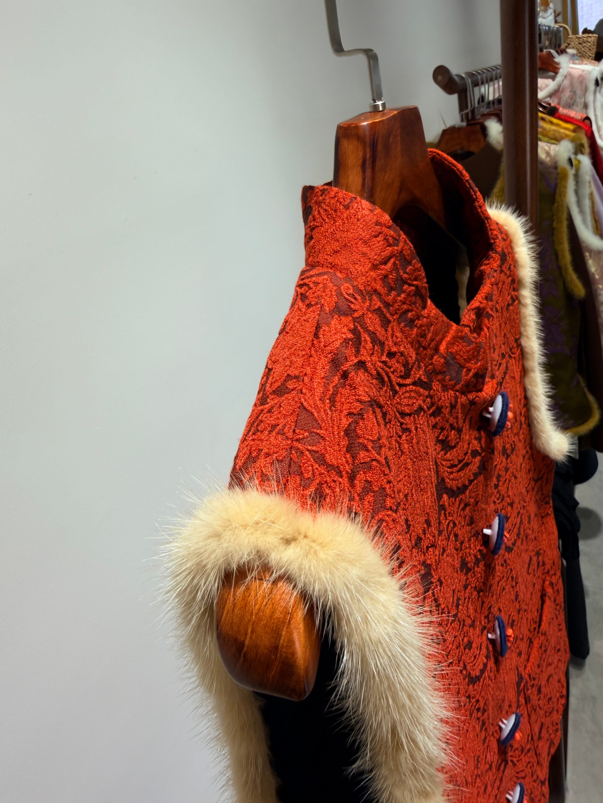 Red textured coat with fur trim on a wooden hanger against a neutral background