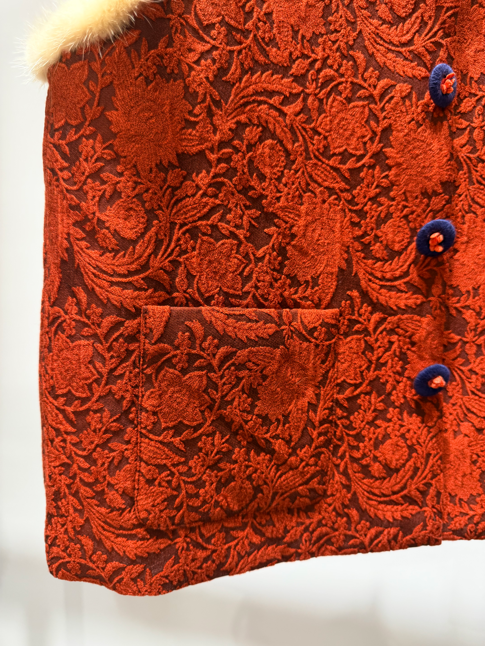 Close-up of a red textured fabric with floral patterns and buttons on a white background