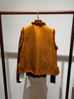 Mustard yellow vest with fur trim hanging on a rack against a white wall.