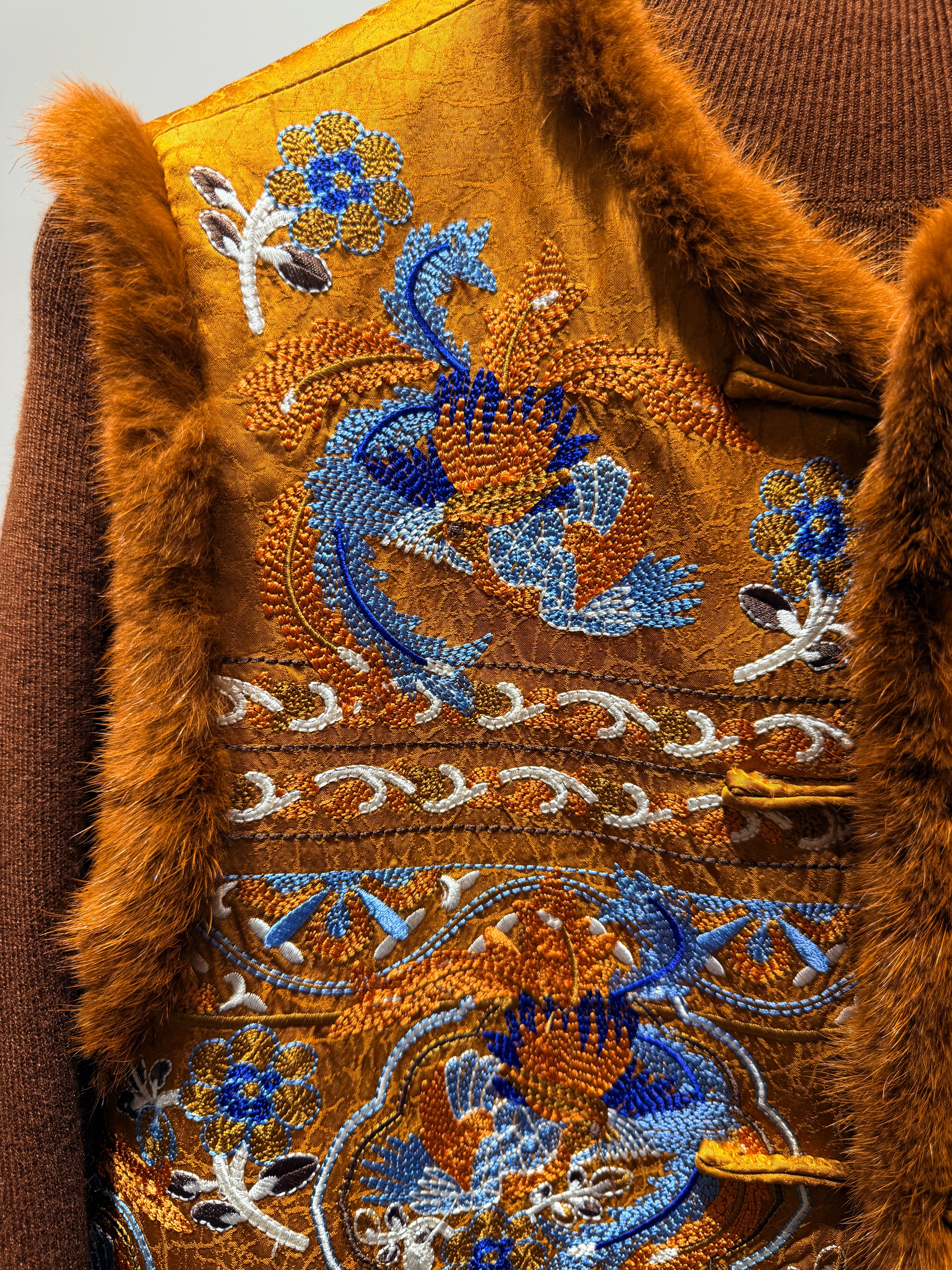 Close-up of a brown garment with intricate blue and white embroidery on a plain background
