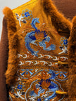 Close-up of a brown garment with intricate blue and white embroidery on a plain background