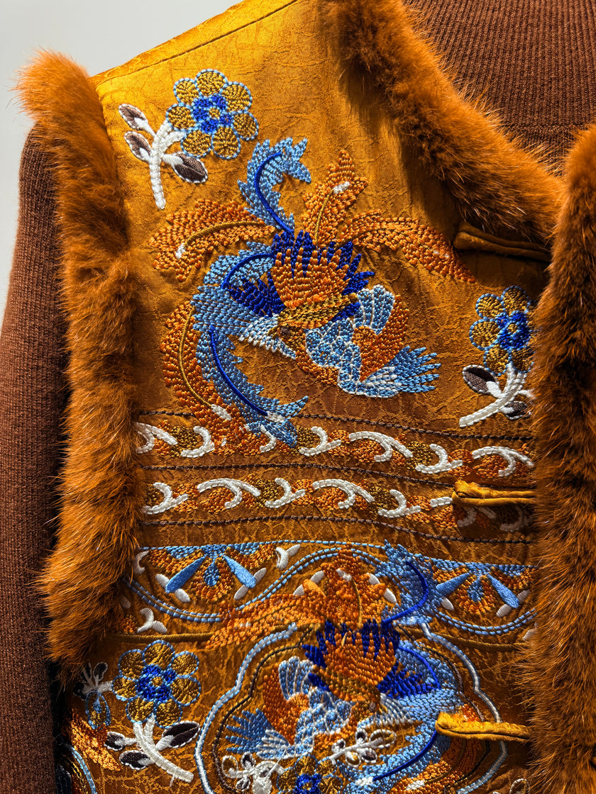 Close-up of a brown garment with intricate blue and white embroidery on a plain background
