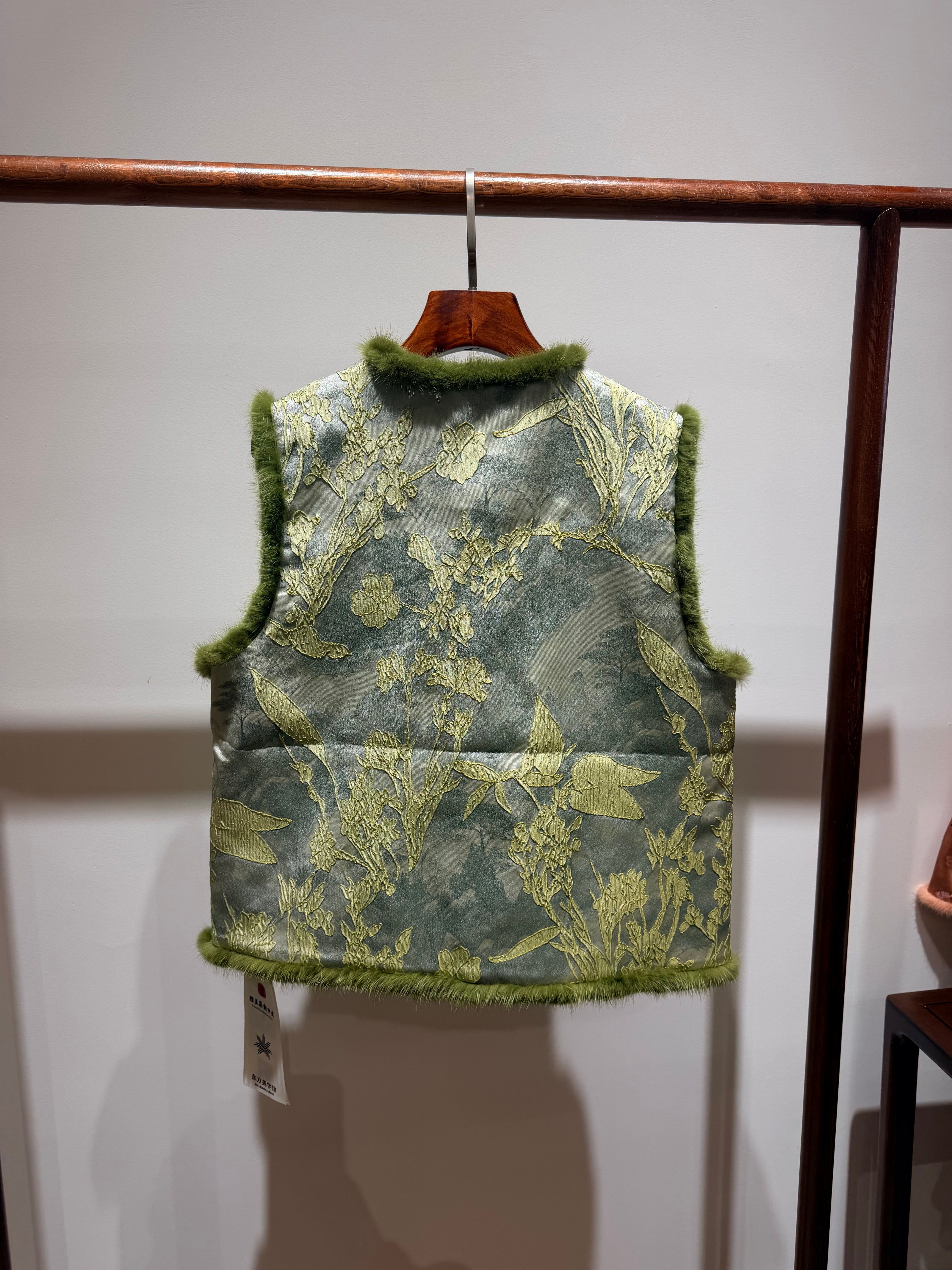 Green floral-patterned vest hanging on a rack against a plain background