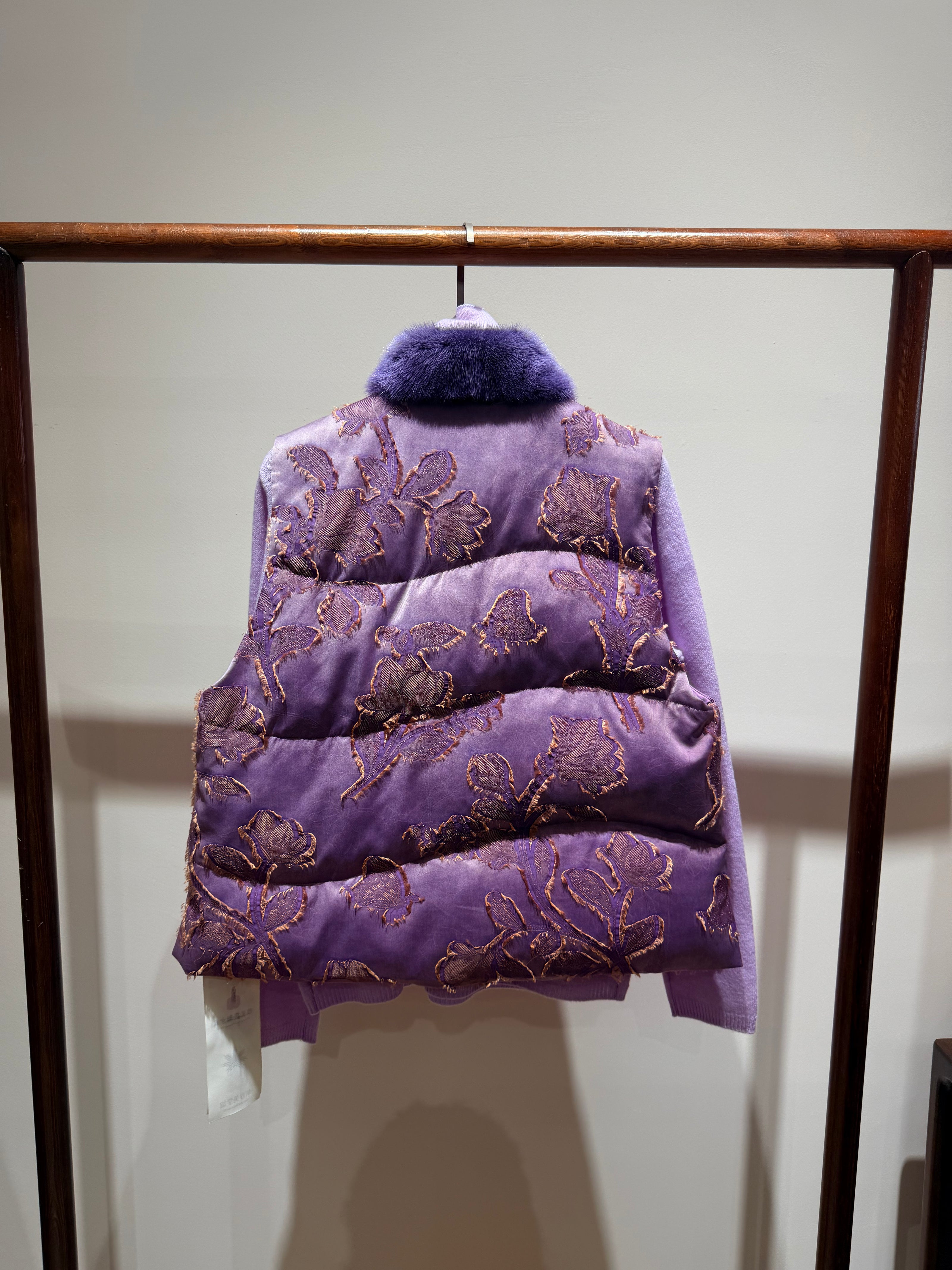 Purple embroidered vest on a wooden rack against a white wall
