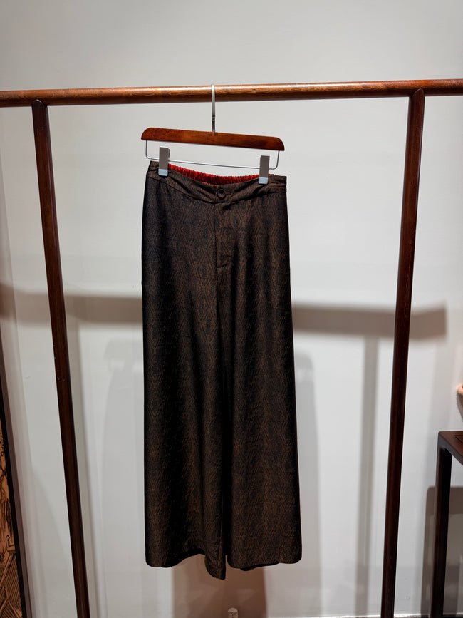 Brown pants hanging on a wooden rack against a white wall
