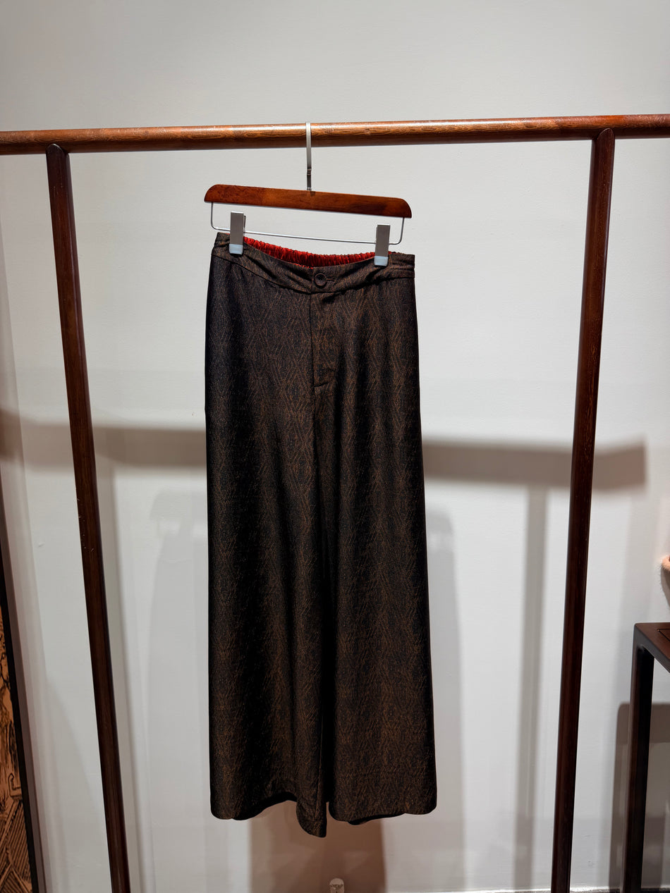 Brown pants hanging on a wooden rack against a white wall