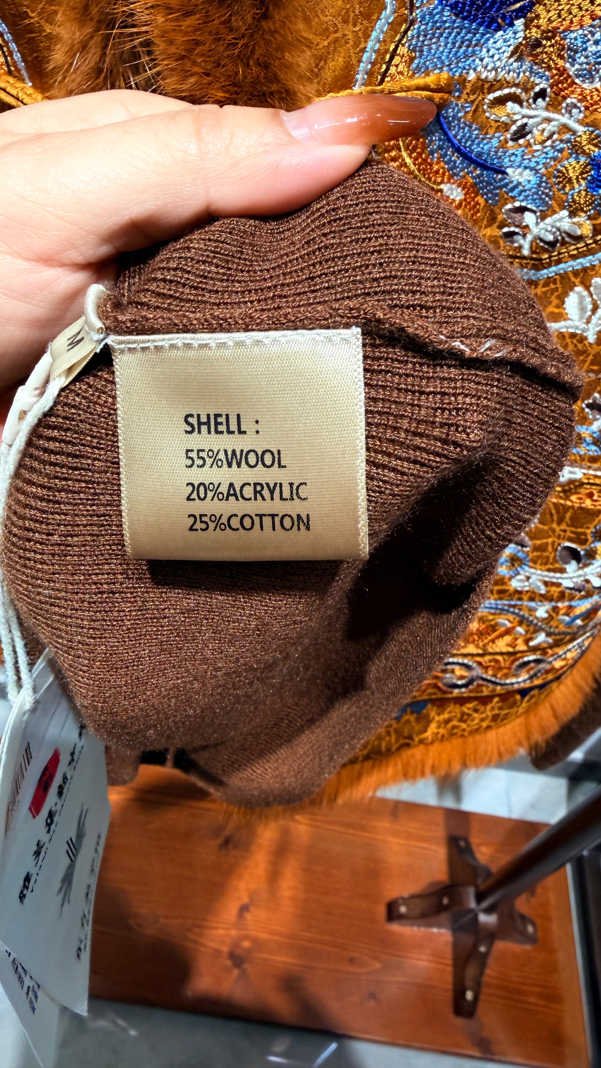 Brown fabric with a label detailing fiber content held by a hand against an embroidered background.