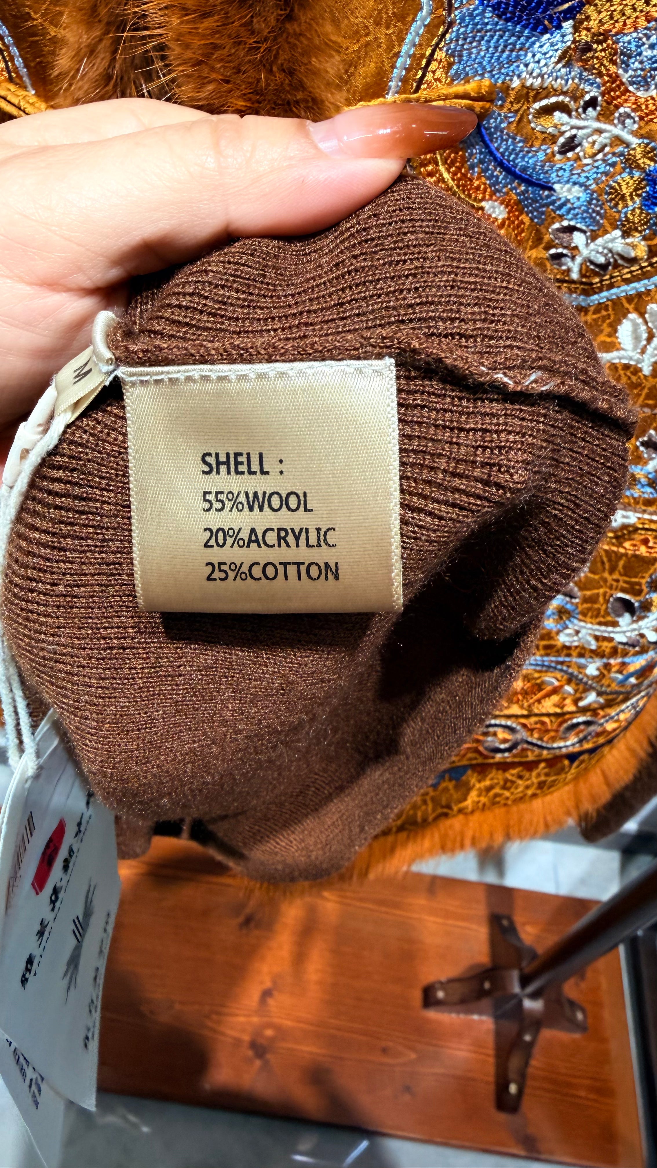 Brown fabric with a label detailing fiber content held by a hand against an embroidered background.
