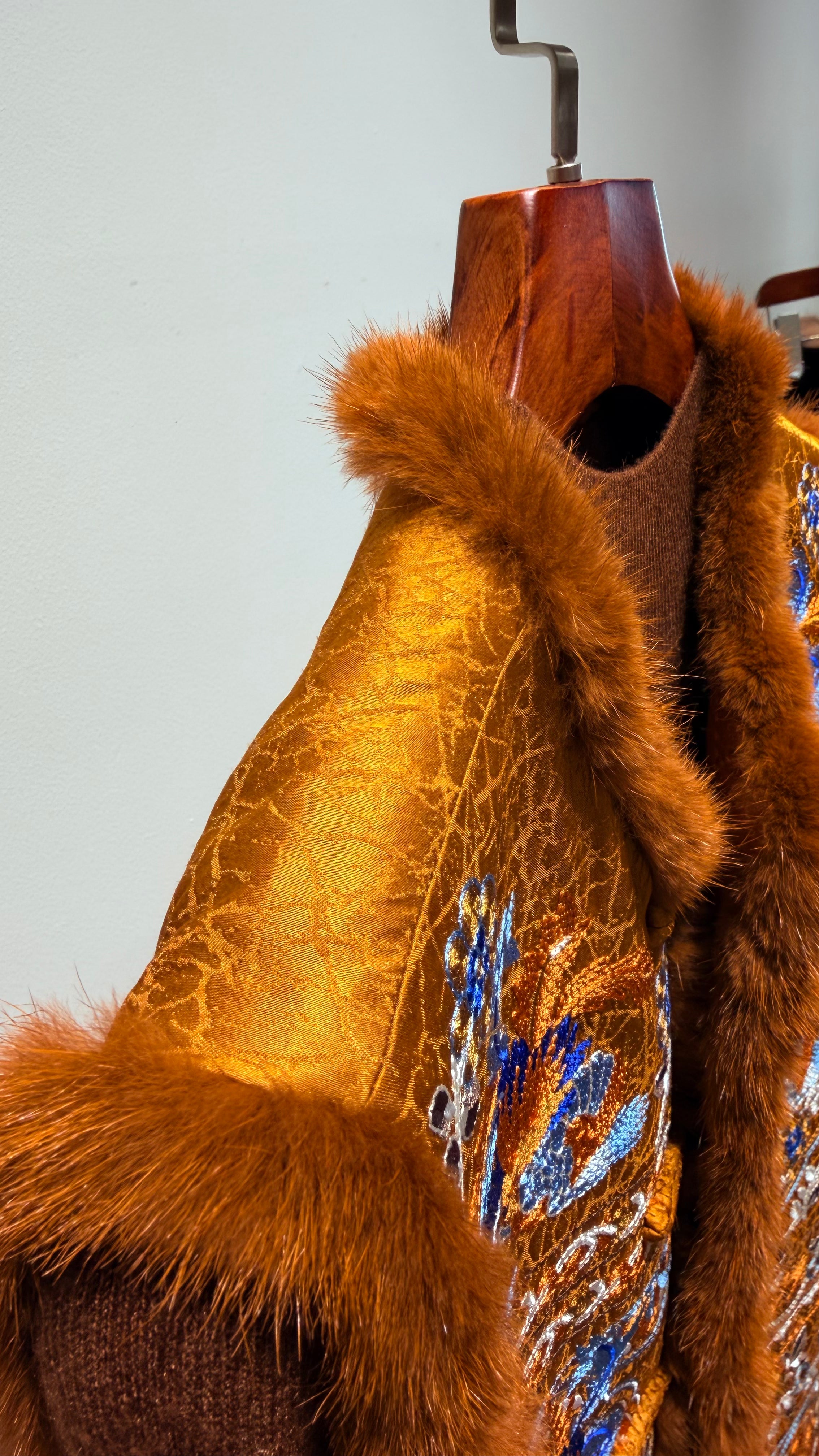Brown fur coat with floral embroidery on a wooden mannequin against a light gray background