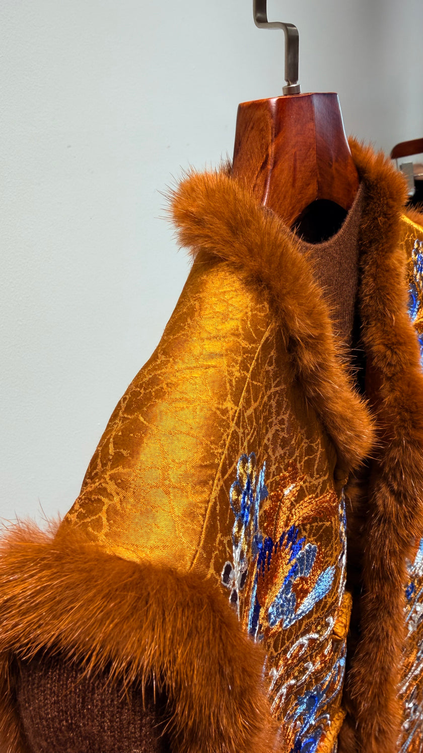 Brown fur coat with floral embroidery on a wooden mannequin against a light gray background
